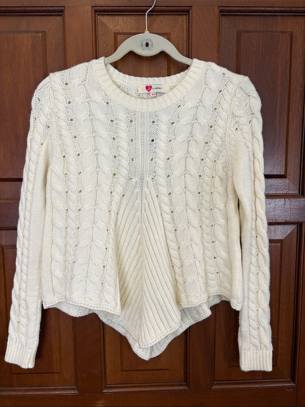Cream cableknit sweater with pointed bottom and lace tie detail on back